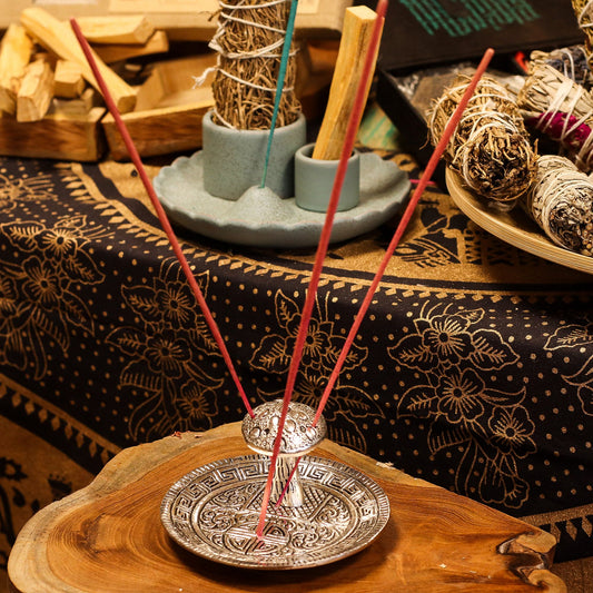 Incense sticks in a holder on a wooden surface with a patterned cloth in the background