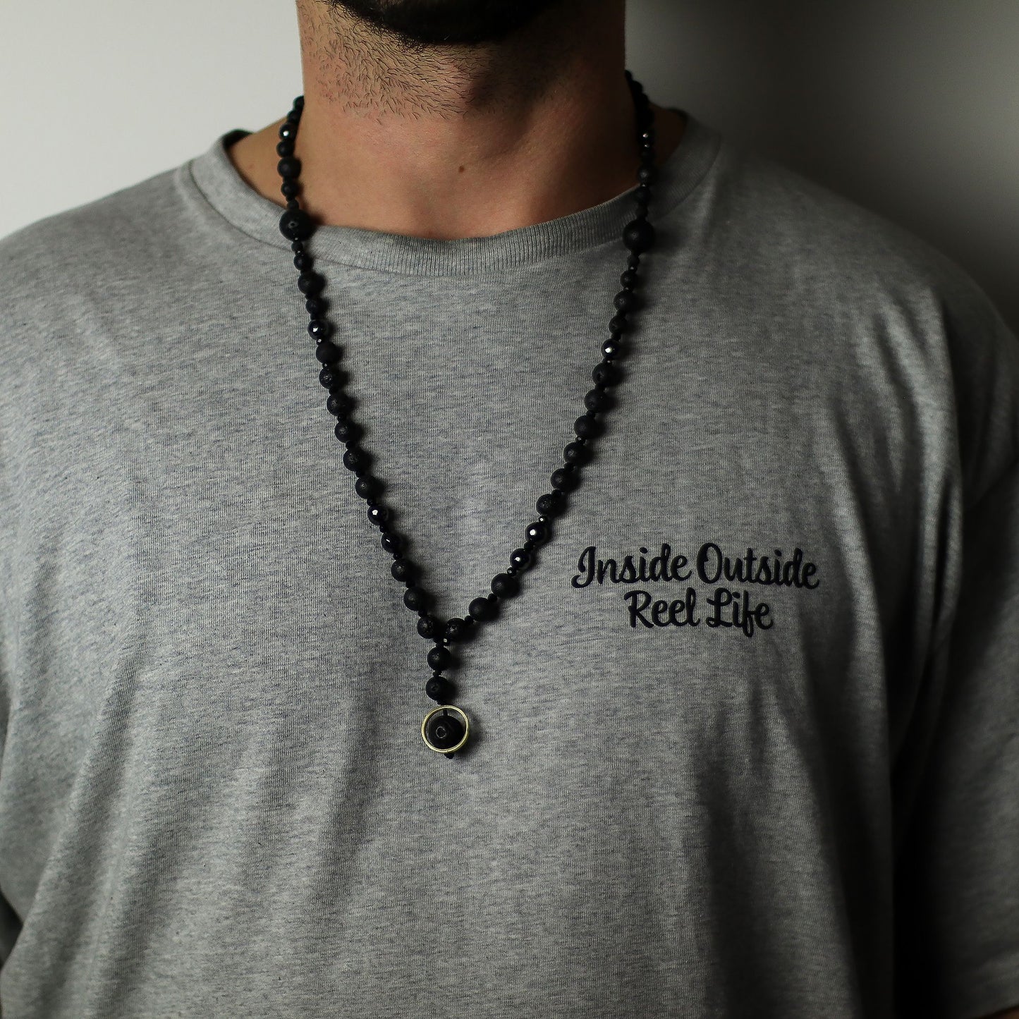 Person wearing a black beaded necklace with a gray t-shirt featuring text.