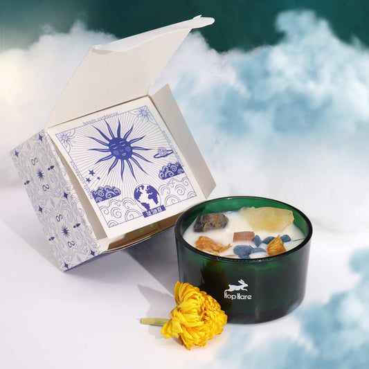 Hop Hare Crystal Magic Flower Candle - The Sun, next to an open box with a sun design, on a cloud background.