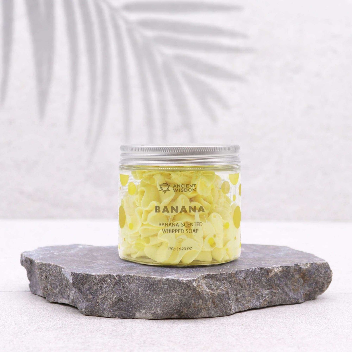 Jar of banana-scented whipped soap on a stone platform with a white background