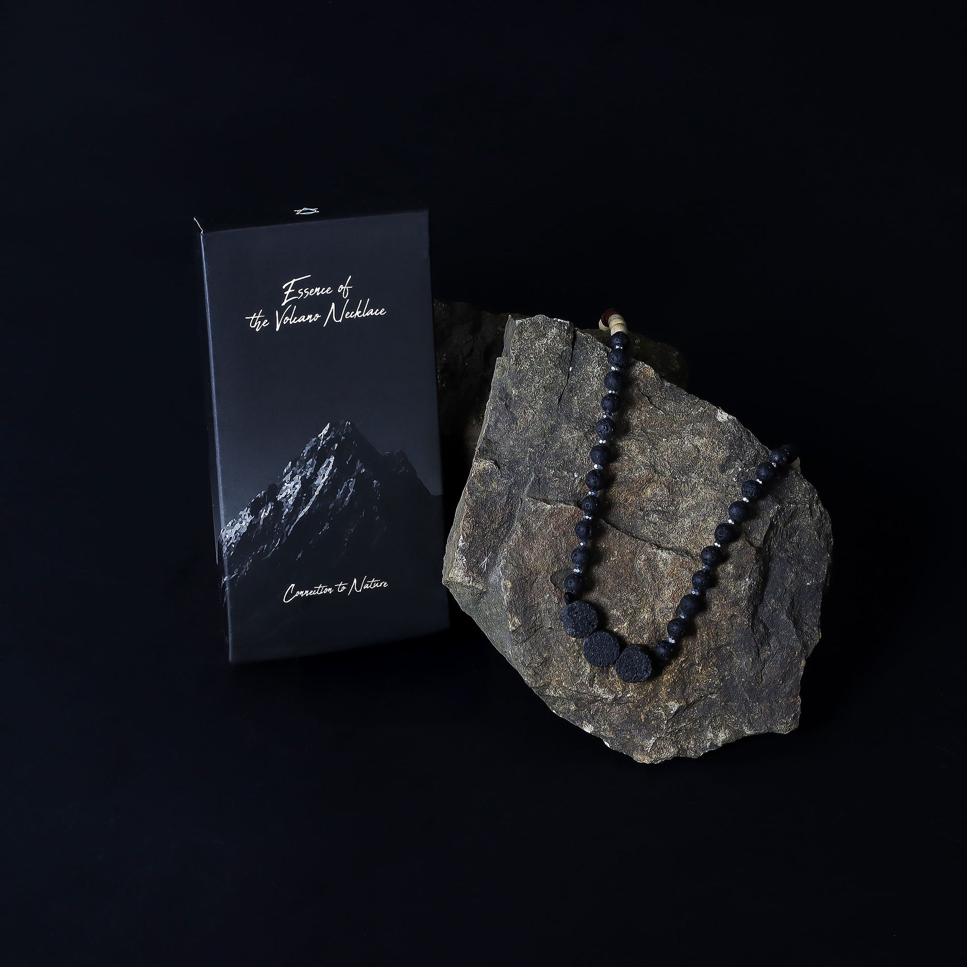 Essence of the Volcano Necklace on a rock with a black box labeled 'Essence of the Numinous' on a dark background