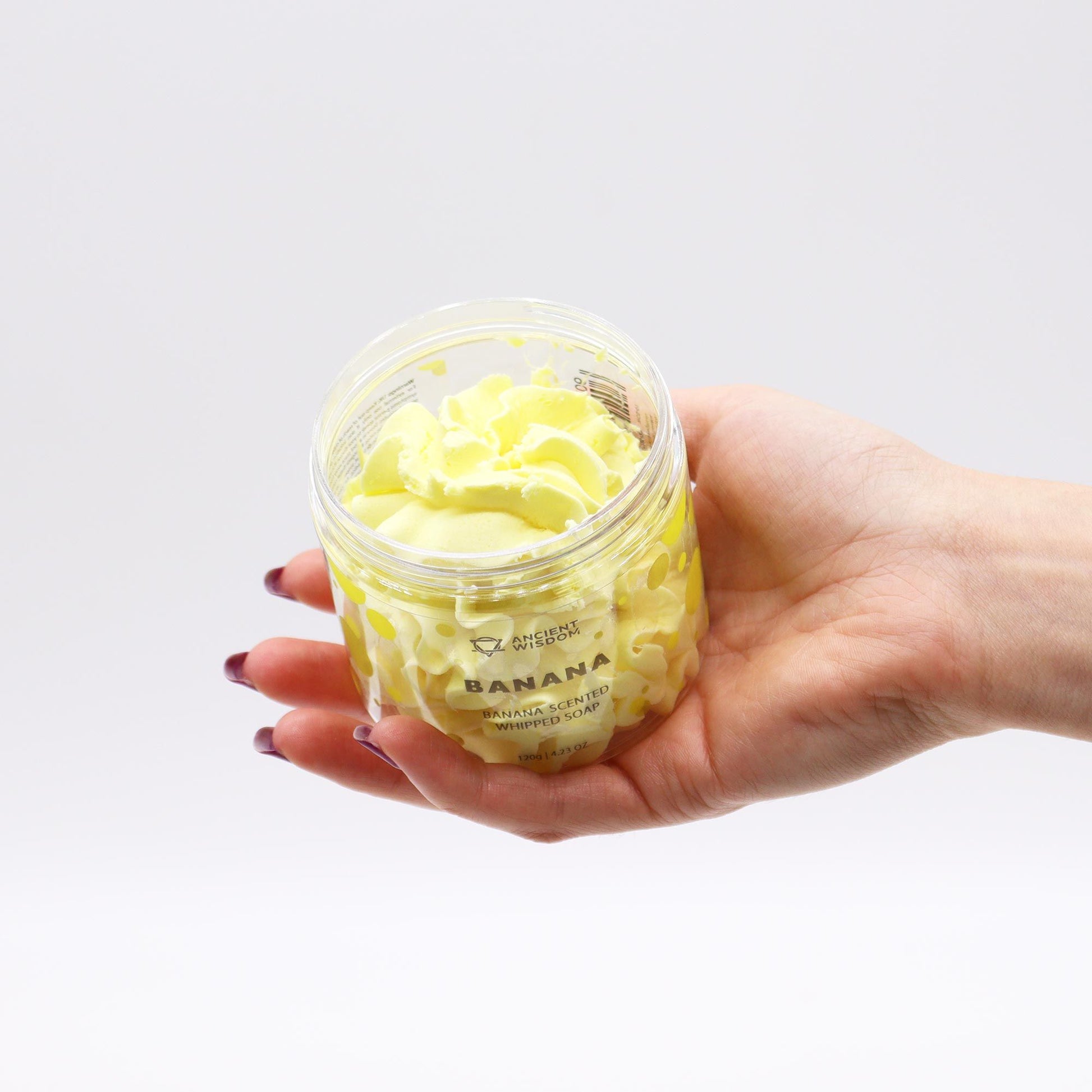 Hand holding a container of Banana Whipped Soap 120g with a white background