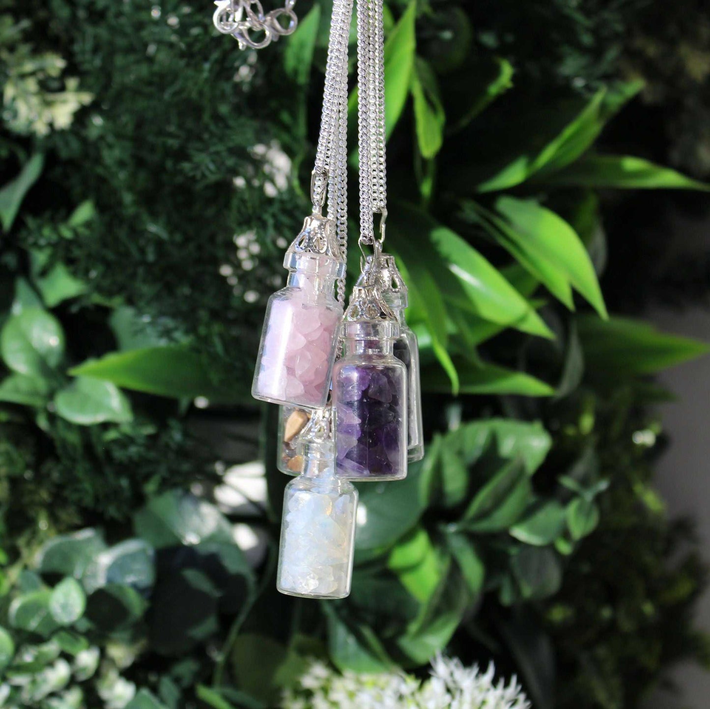 Necklace with three small glass bottles containing different colored stones against a green leafy background