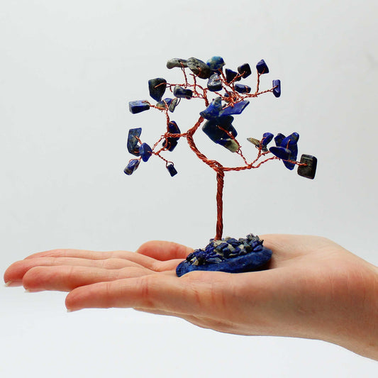 Hand holding a small tree sculpture with blue stones against a white background