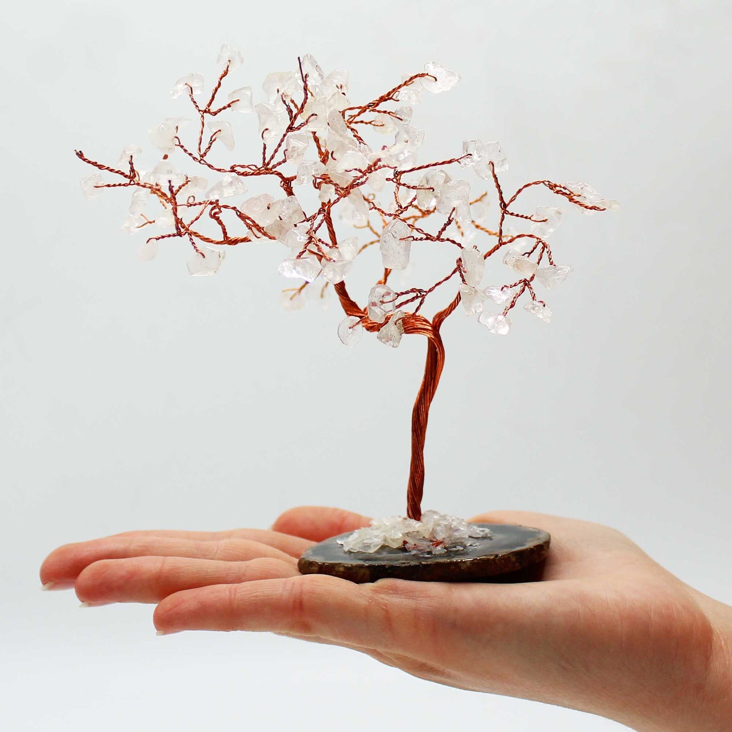 Small decorative tree with red branches and white beads on a hand against a light gray background