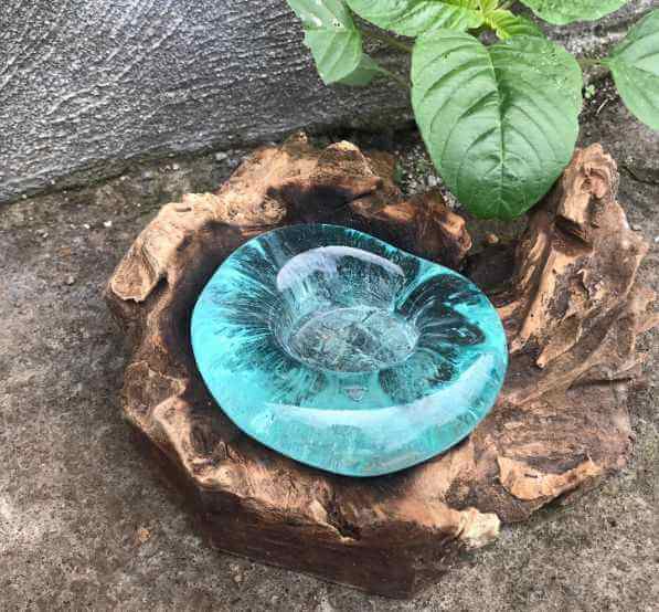 Turquoise glass bowl on a natural wooden base with green leaves in the background