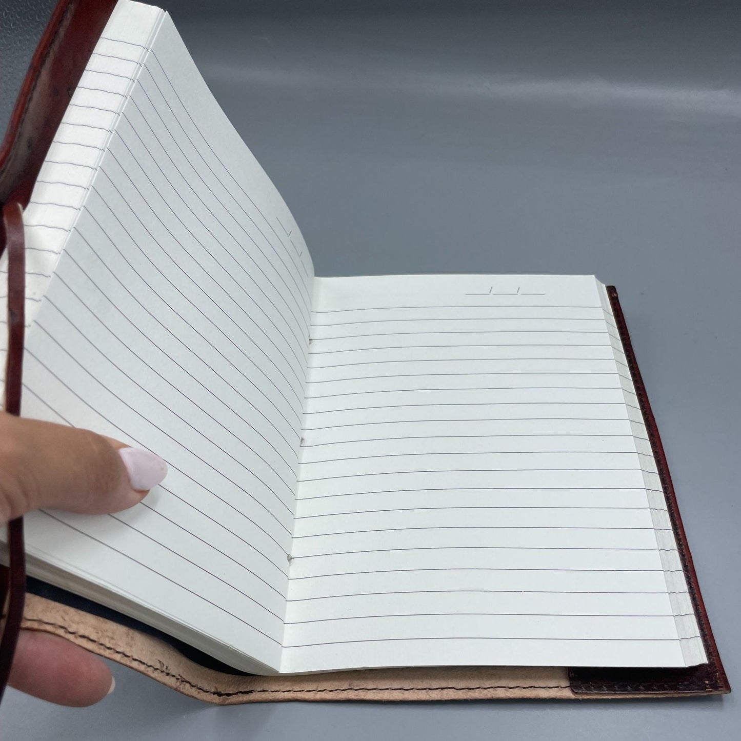 Open notebook with lined pages held by a hand on a gray background