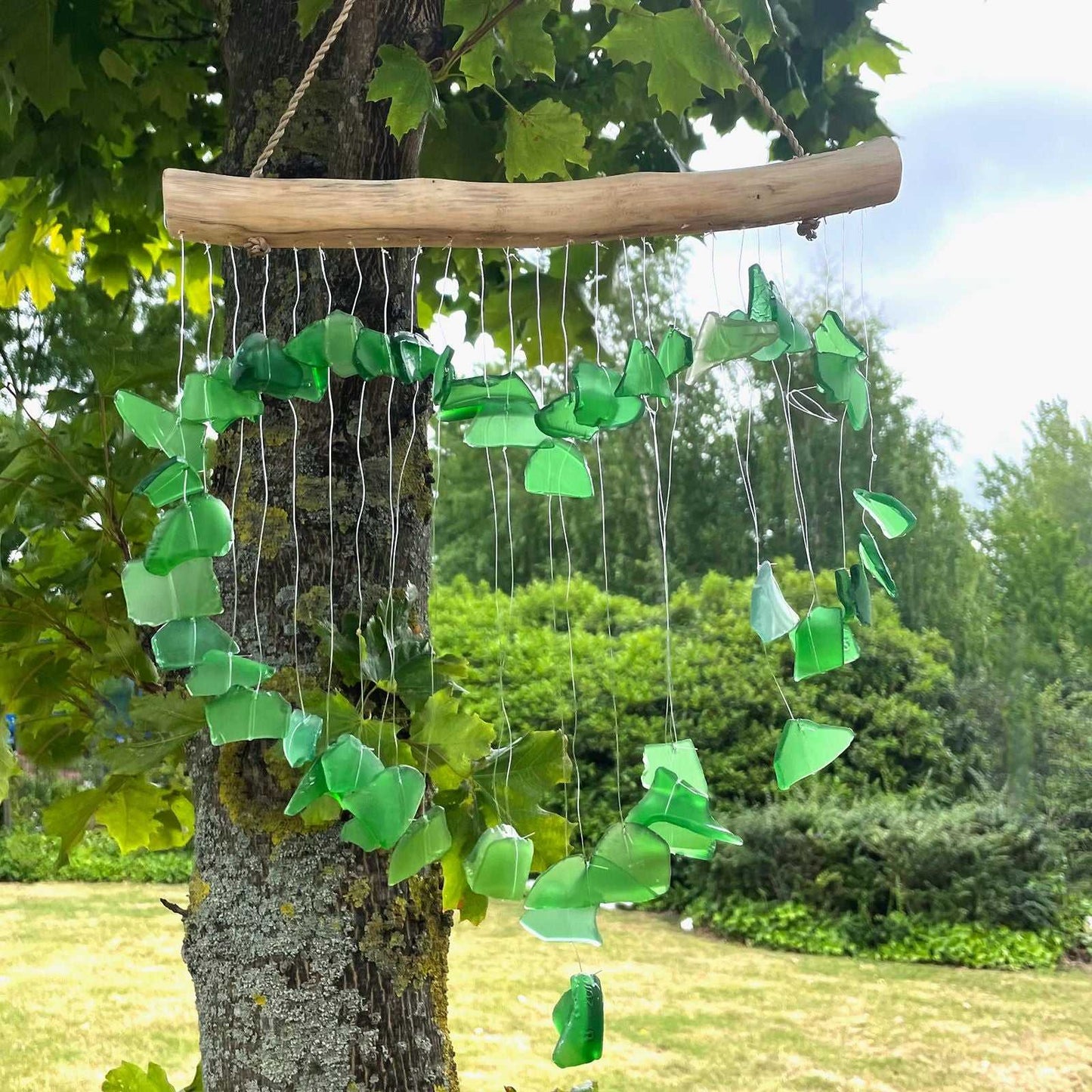 Green glass wind chime hanging from a tree in a garden setting