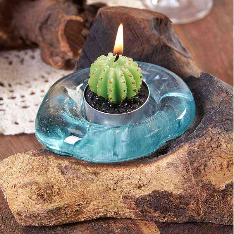 Decorative candle with cactus design in a molten blue glass holder on a wooden surface