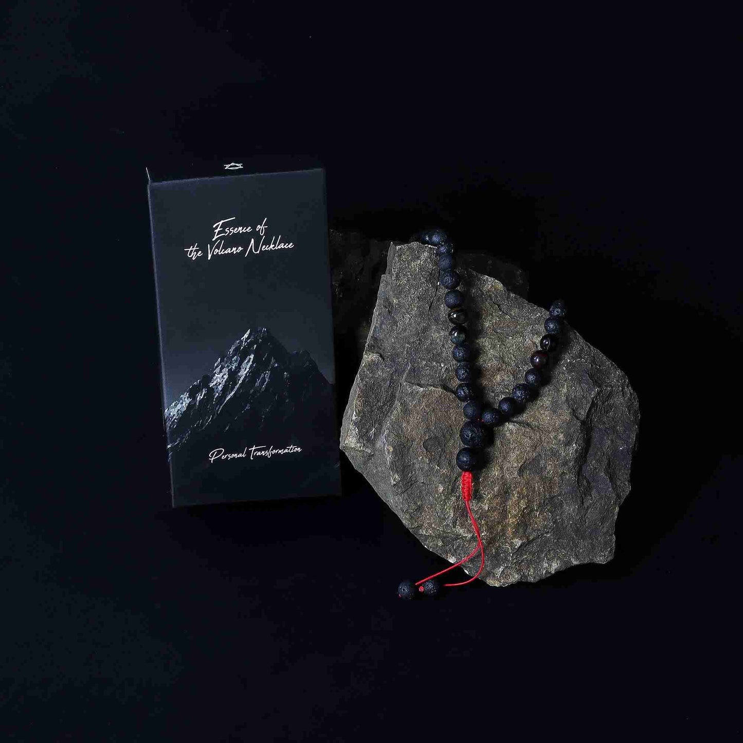Black beaded necklace with red cord on a rock next to a black box with mountain design