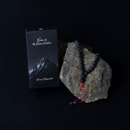 Black beaded necklace with red cord on a rock next to a black box with mountain design