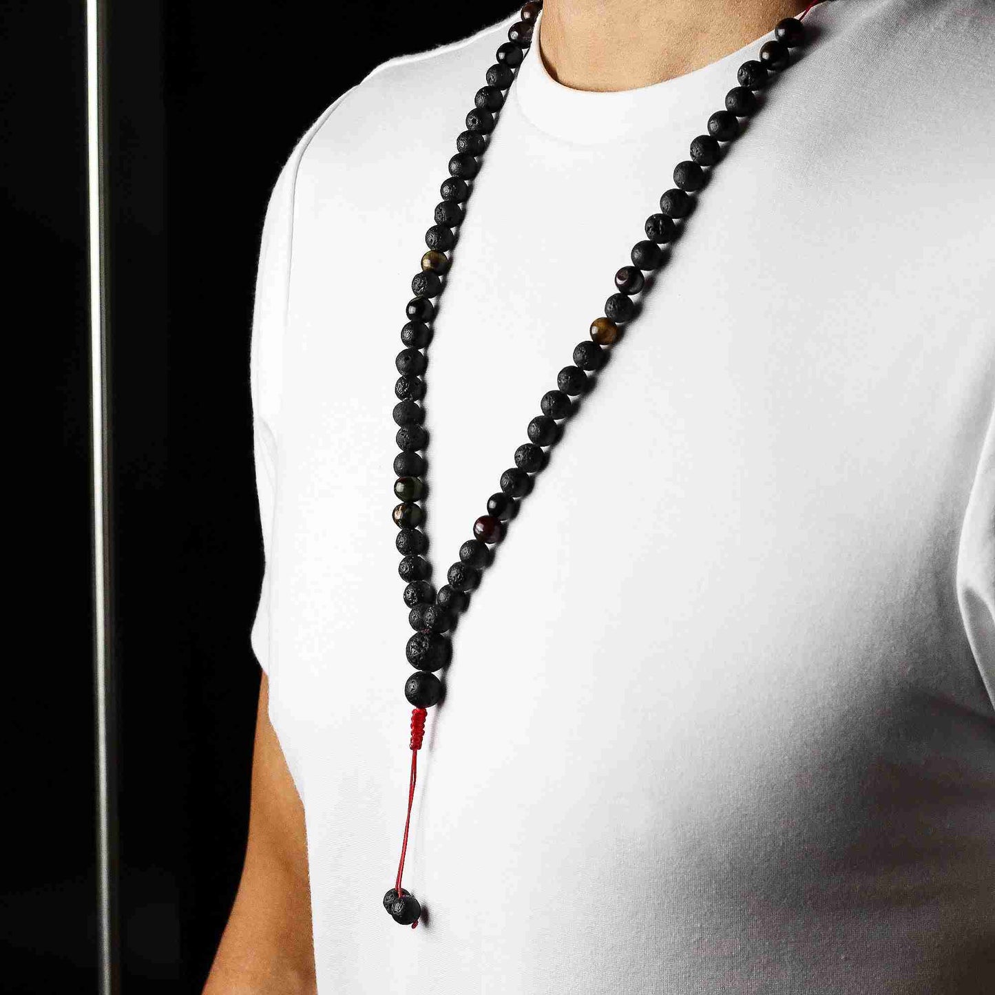 Person wearing a black beaded necklace against a white shirt and black background