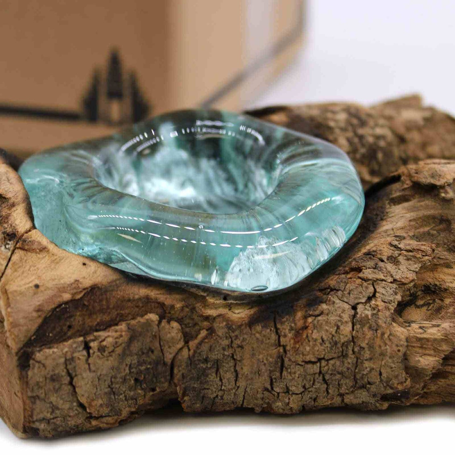 Turquoise molten glass bowl on a wooden log