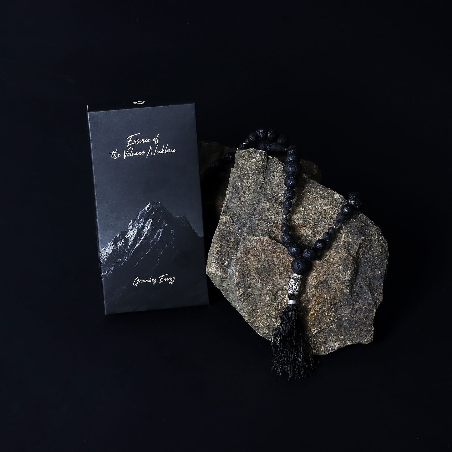 Essence of the Volcano Necklace with tassel on a rock next to a mountain-themed card on a black background