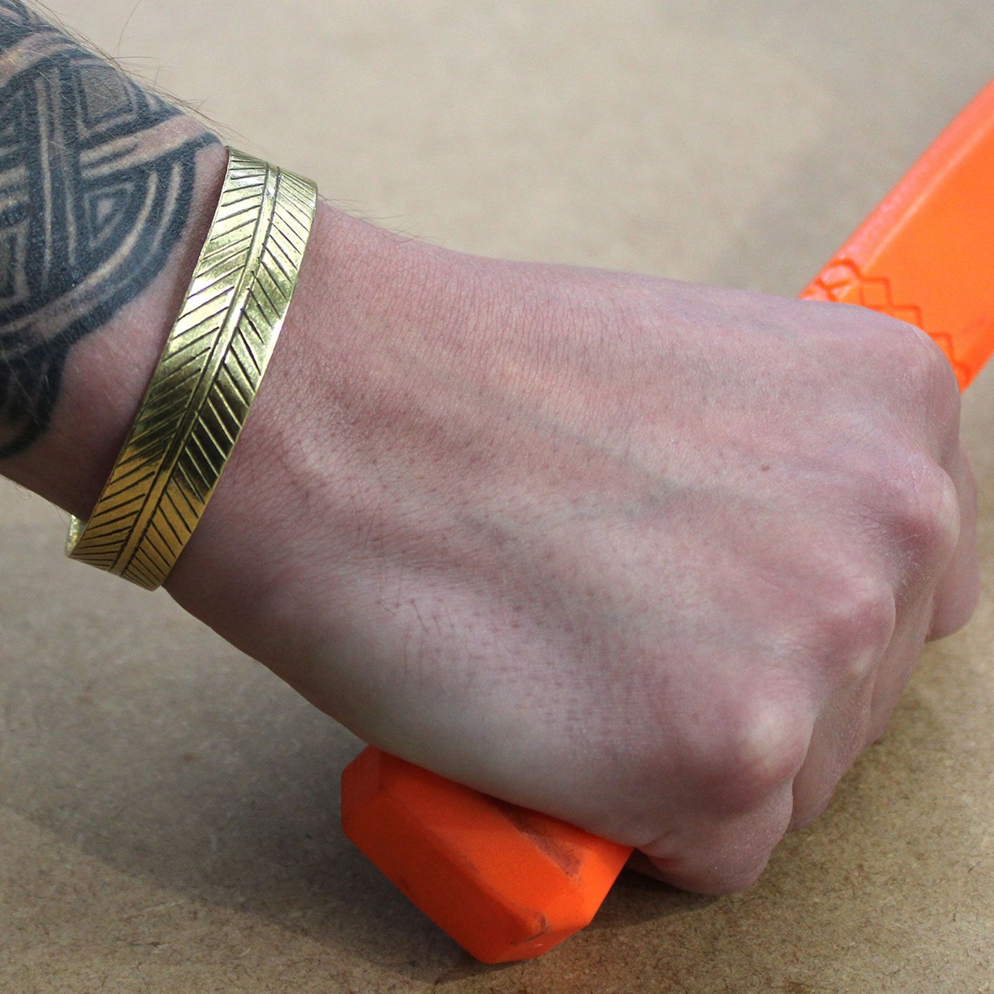 Hand holding an orange object with a Brass Tibetan Bracelet - Wide Tribal Leaf on a beige background