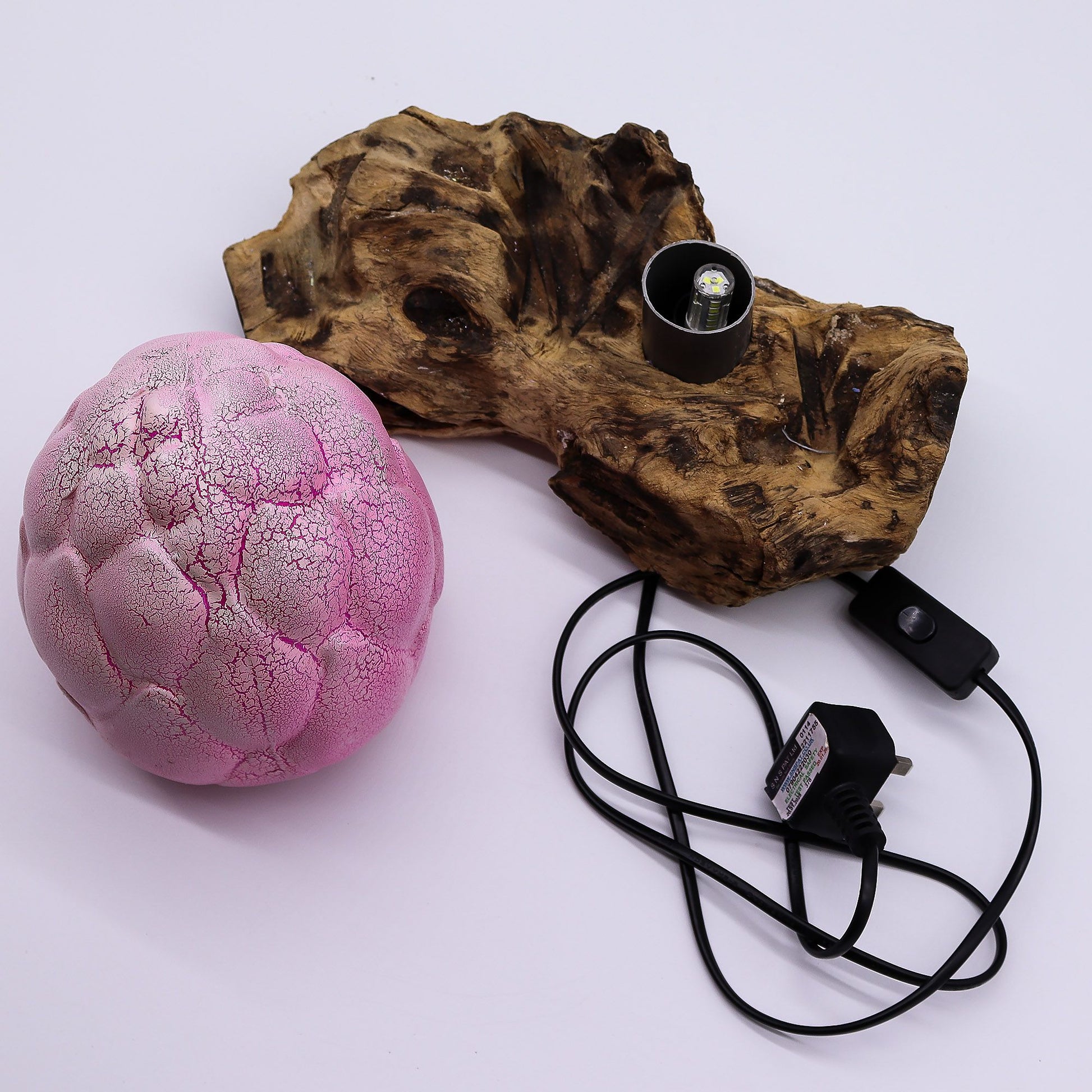 Pink textured sphere, wooden block with light bulb, and power cord on a white background