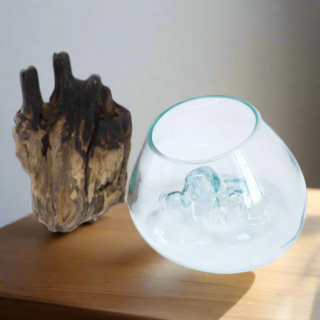 Clear glass bowl with decorative stones next to a piece of driftwood on a white background