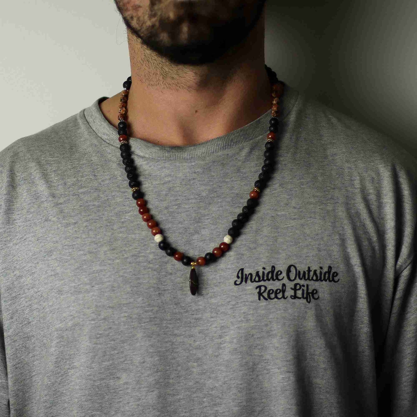 Person wearing a gray t-shirt with 'Inside Outside Reel Life' text and a beaded necklace.