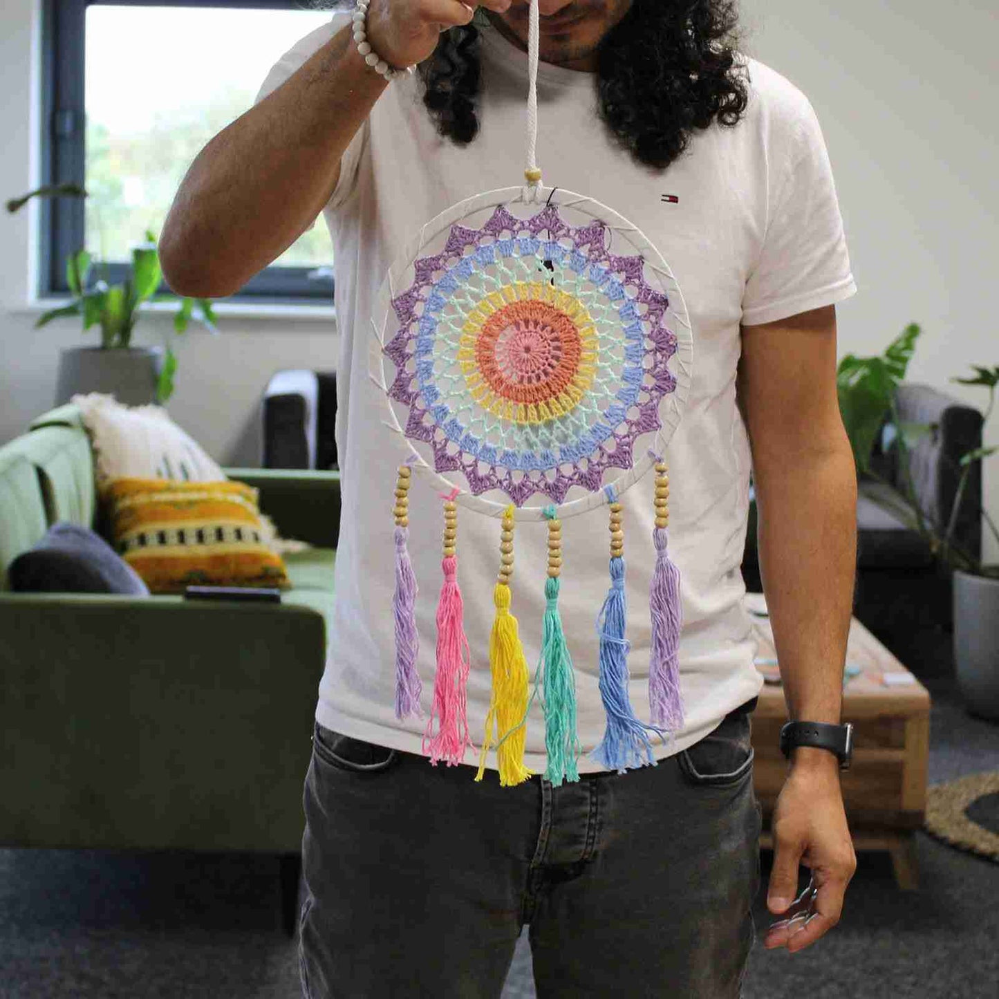 A person wearing a white T-shirt holding a rainbow dreamcatcher. 
